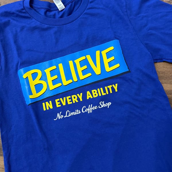 Blue t-shirt with "BELIEVE IN EVERY ABILITY No Limits Coffee Shop" in yellow and white text.