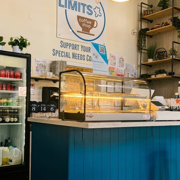 A coffee shop interior with a blue counter, display case, drink refrigerators, and shelves with plants.