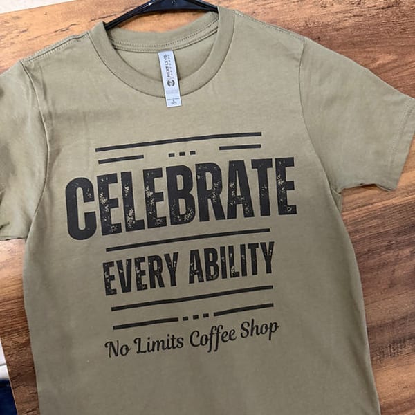 Olive green t-shirt with "CELEBRATE EVERY ABILITY No Limits Coffee Shop" in black text.