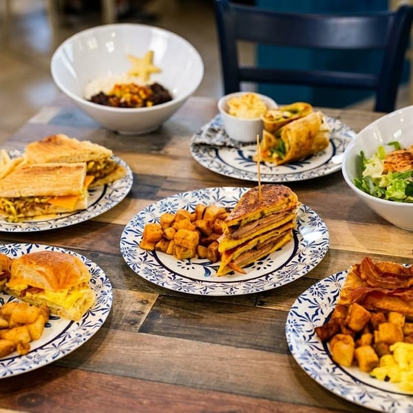 A wooden table laden with various breakfast and lunch dishes on blue and white plates.