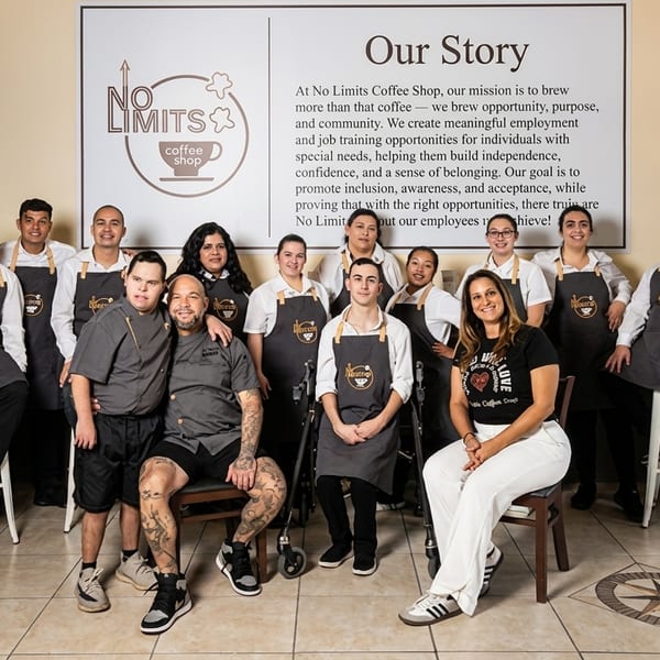 The diverse staff of No Limits Coffee Shop, including individuals with disabilities, smiling in their aprons.